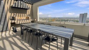 Un patio al aire libre con mesa y sillas, una parrilla y vistas a un paisaje urbano.
