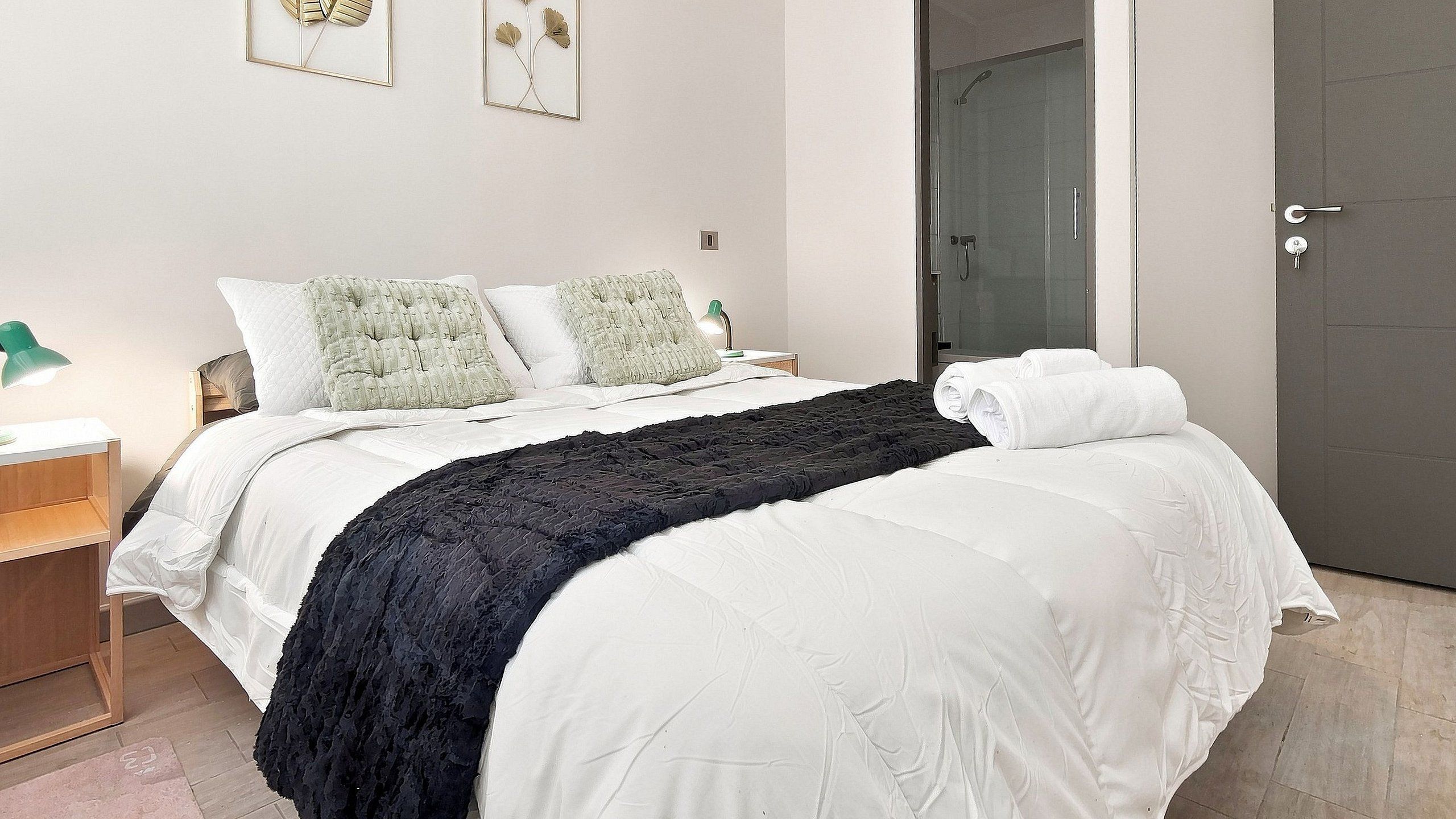 A hotel room with a bed, a nightstand, a lamp, and a door.