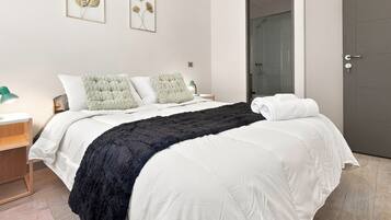 A hotel room with a bed, a nightstand, a lamp, and a door.