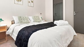A hotel room with a bed, a nightstand, a lamp, and a door.