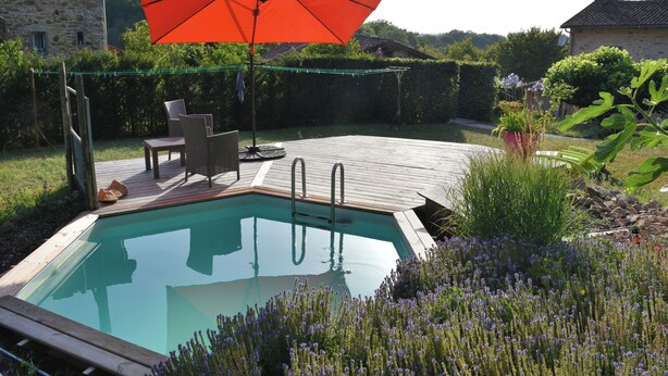 Una piscina con muelle de madera, una silla y una sombrilla.
