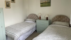 A bedroom with two single beds, a nightstand with lamps, a dresser, and framed pictures on the wall. - Central location, Its our home away from home unique, cosy and charming. (Boat of Garten)
