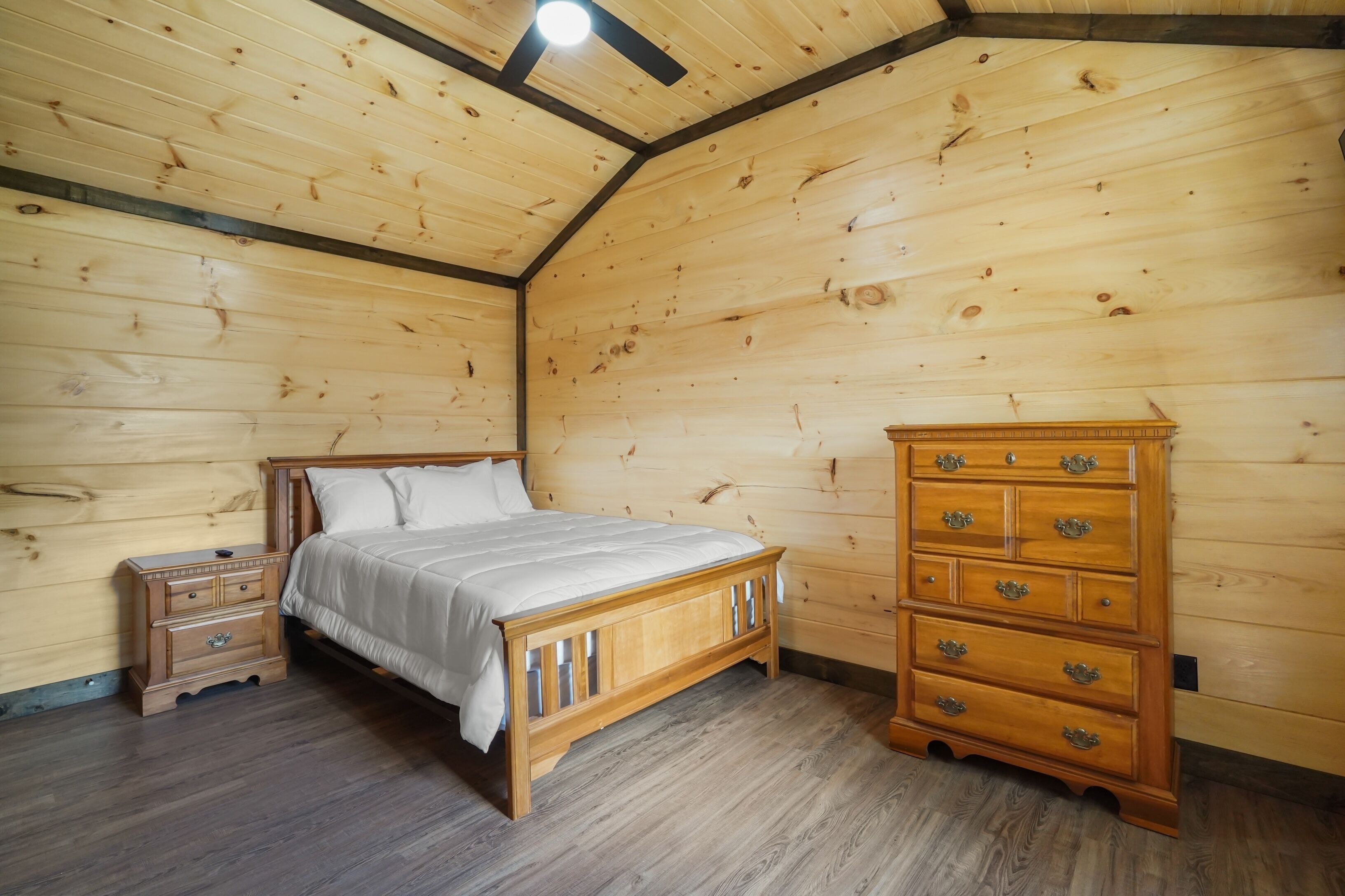 Une chambre à coucher aux murs lambrés, comprenant un lit, une table de chevet, une commode et un plafond en pente.