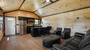Un intérieur de chalet chaleureux avec un plafond en bois, un coin cuisine, un canapé et un espace bar.