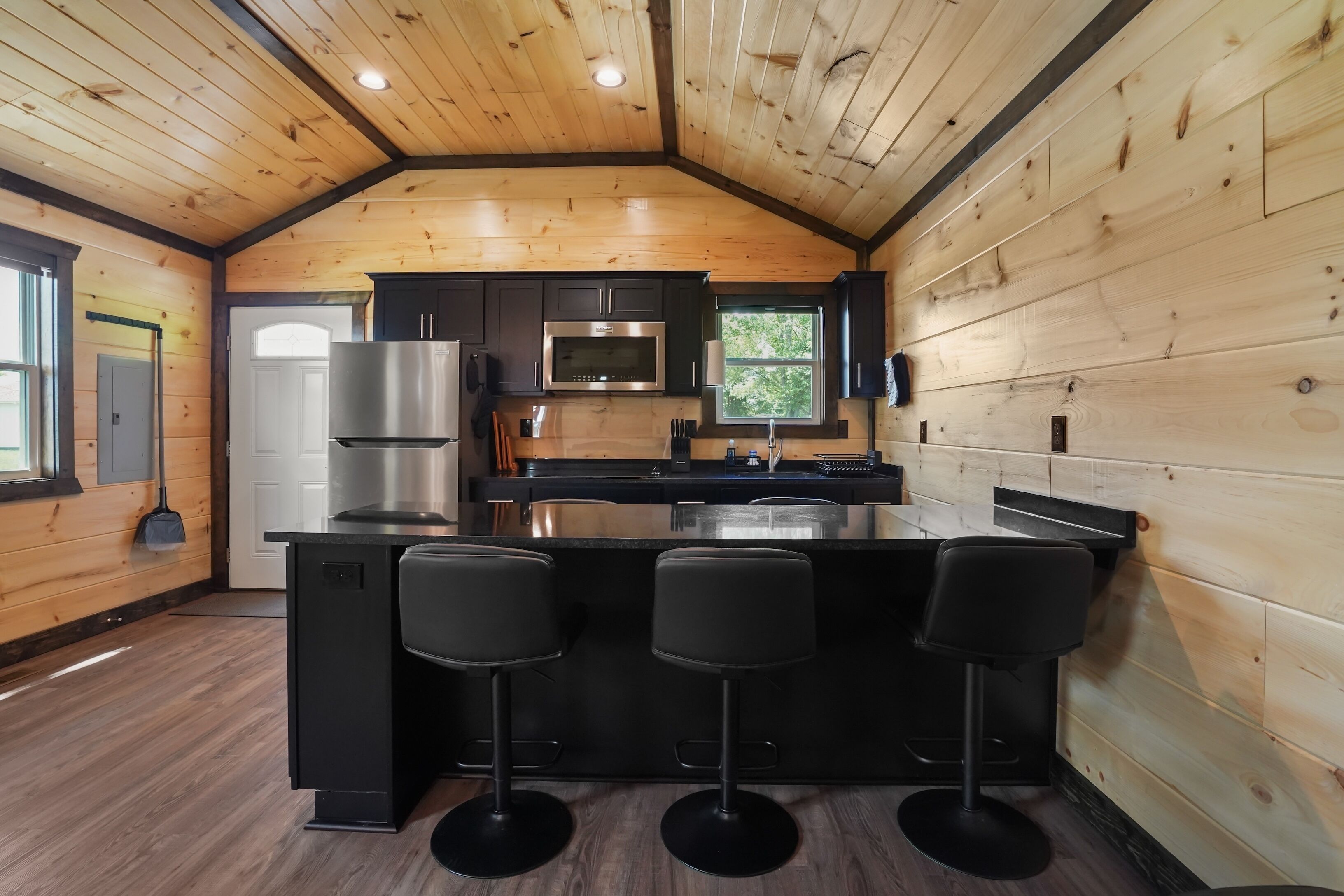 A kitchen with wooden walls, a black countertop, and three bar stools.