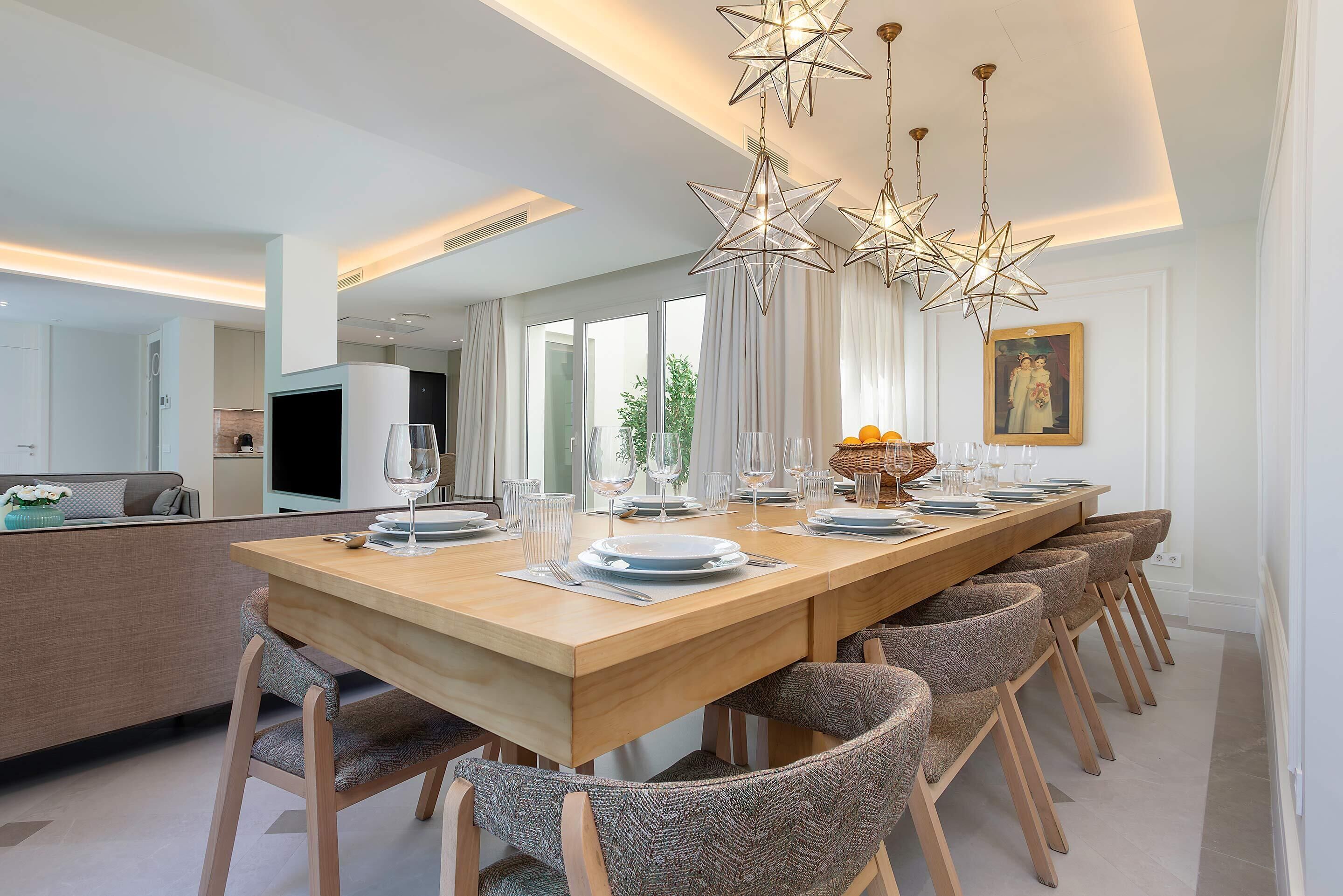 Een moderne eetruimte met een lange houten tafel, meerdere stoelen en hanglampen in de vorm van sterren.