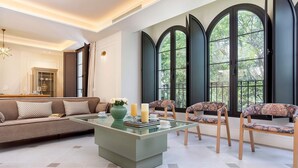 Un salon moderne avec un canapé, des fauteuils, une table basse en verre et de grandes fenêtres.