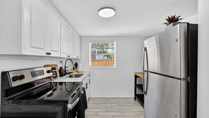 A modern kitchen with white cabinets, a stainless steel refrigerator, and a window with blinds. - Cozy 1-bedroom house in lovely Tampa with AC - 2706C (Tampa)