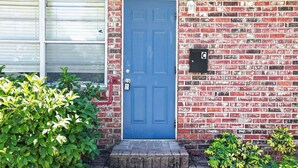 A blue door with a mail slot, a brick wall, and a small step leading to the entrance. - Cozy 1-bedroom house in lovely Tampa with AC - 2706C (Tampa)