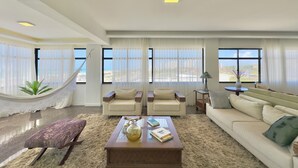 Ein geräumiges Wohnzimmer mit großem Fenster, einer Hängematte und Blick auf die Stadt.