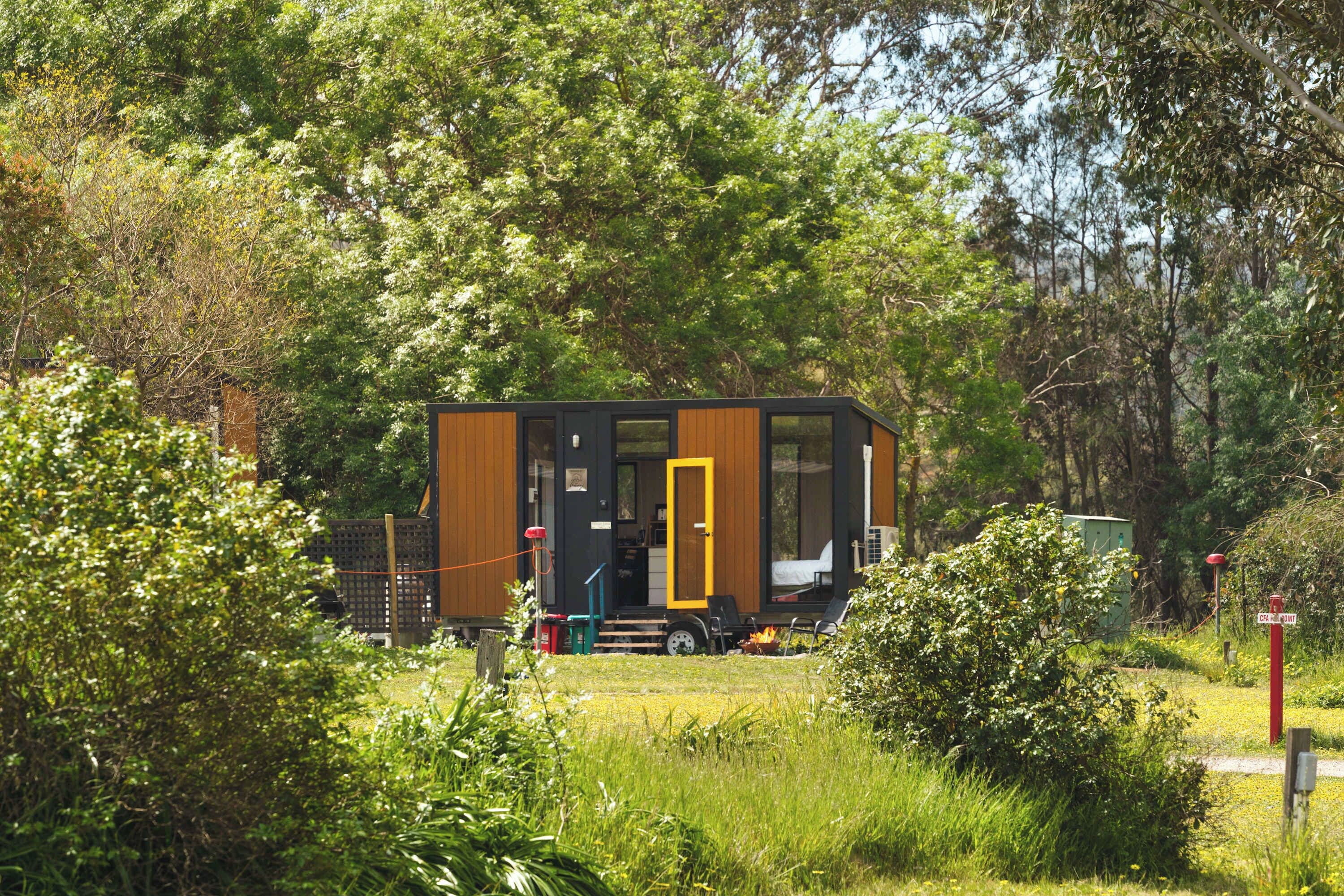 Een kleine, moderne vakantiebungalow met een grote schuifdeur, omgeven door weelderige begroeiing.