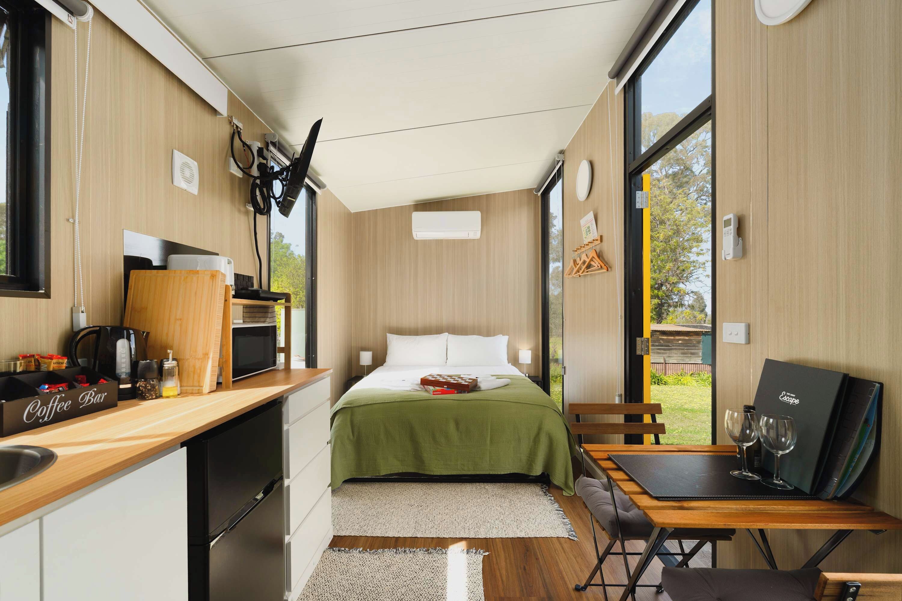 A compact room with a bed, a small kitchenette, a dining area, and a large window providing a view of the outdoors.