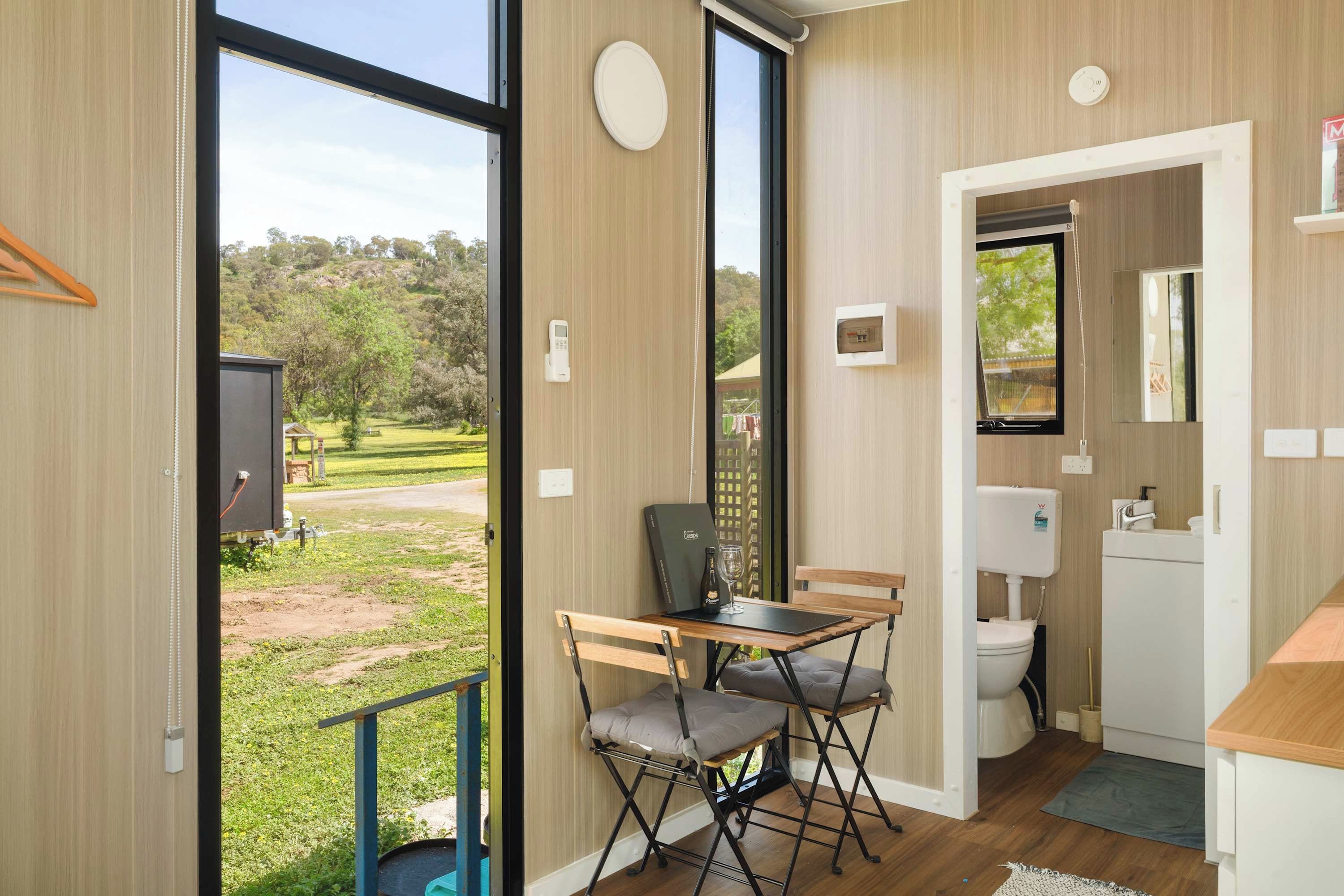 A modern room with a large window, a small table with a chair, a toilet, and a sink.