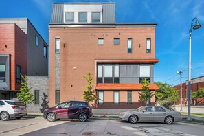 A modern building with a brick facade, large windows, and a parking lot with two cars. - Rooftop Deck | Downtown CLE | Near ClevelandClinic (Cleveland)