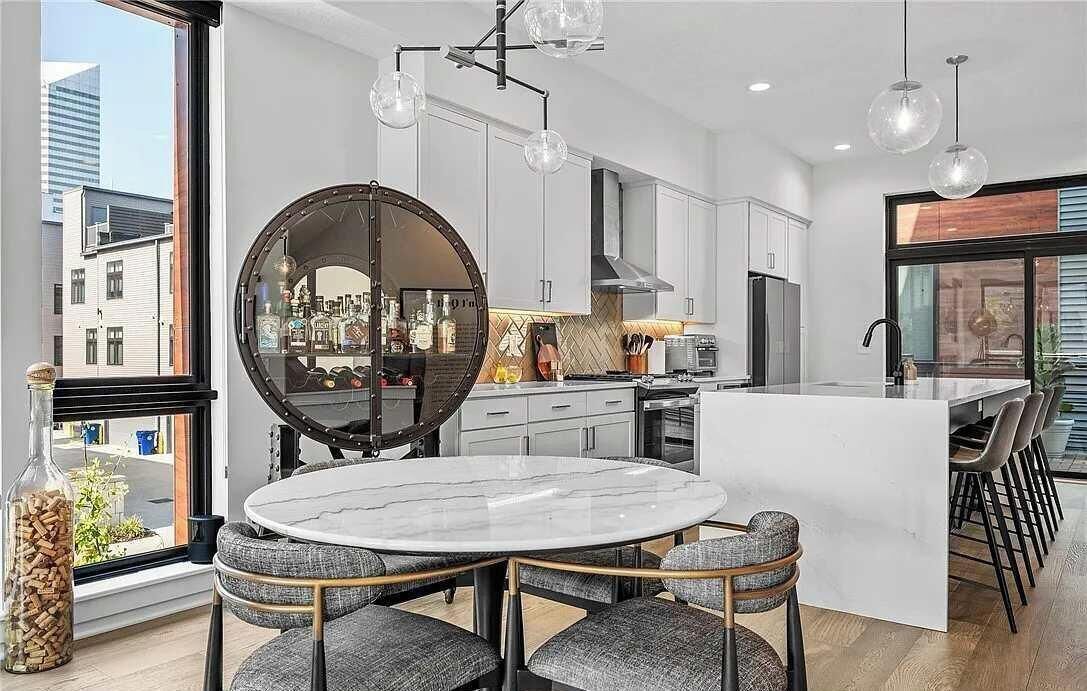 A modern kitchen with a round mirror, white cabinets, and a dining area with a marble table and grey upholstered chairs.