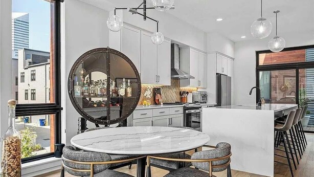 A modern kitchen with a round mirror, white cabinets, and a dining area with a marble table and grey upholstered chairs. - RoofTop - Sleeps 12 - Downtown CLE (Cleveland)