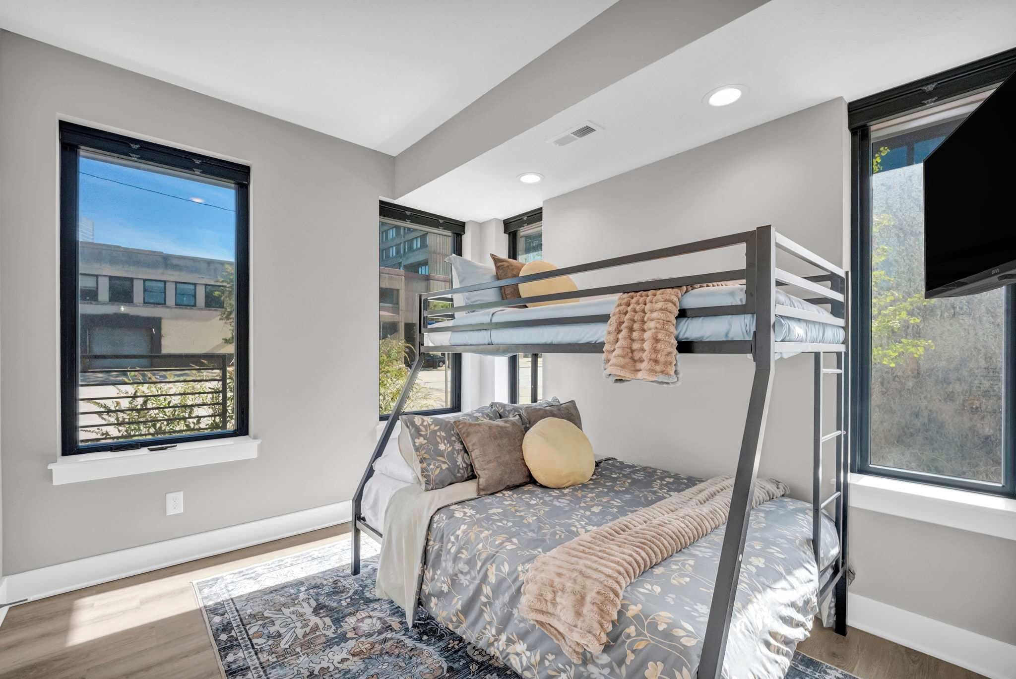 A modern bedroom with a bunk bed, large windows, and a flat-screen TV.