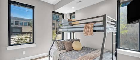 A modern bedroom with a bunk bed, large windows, and a flat-screen TV.
