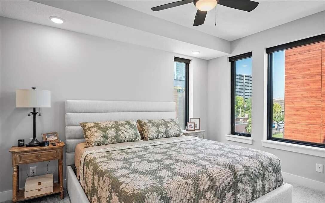 A bedroom with a bed, bedside tables, a ceiling fan, and large windows.