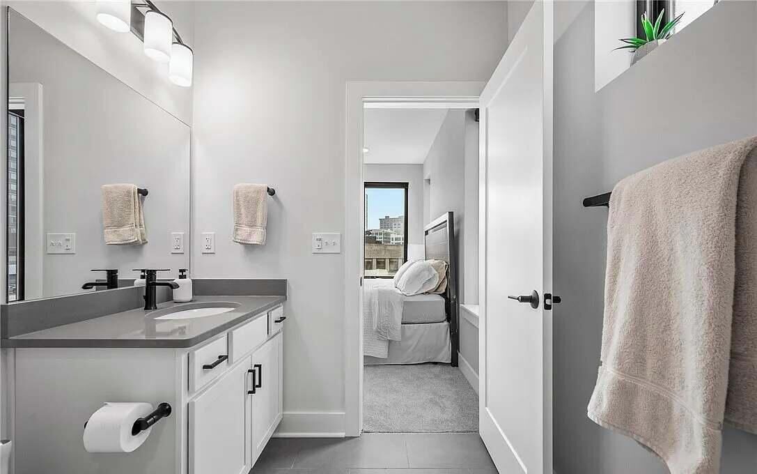 A modern bathroom with a large mirror, a sink, and a toilet. There is a towel hanging on the wall and a towel rack by the door.