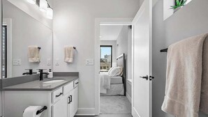A modern bathroom with a large mirror, a sink, and a toilet. There is a towel hanging on the wall and a towel rack by the door. - RoofTop - Sleeps 12 - Downtown CLE (Cleveland)