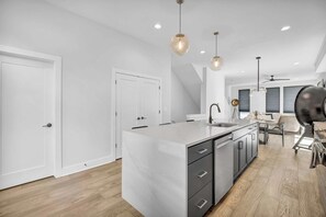 A modern kitchen with a central island, pendant lighting, and a dining area with a table and chairs. - Rooftop Deck | Downtown CLE | Near ClevelandClinic (Cleveland)
