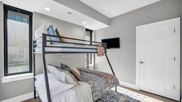 A bunk bed with a TV mounted on the wall above it, a door on the right, and a window on the left.