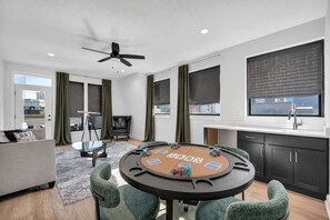 A modern living room with a round table, green chairs, a sofa, a black leather chair, a ceiling fan, and a window with a view of buildings. - Rooftop Deck | Downtown CLE | Near ClevelandClinic (Cleveland)