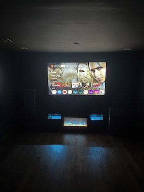 Een donkere kamer met een groot scherm waarop een tv-interface staat, een kleine televisie eronder en een houten vloer.