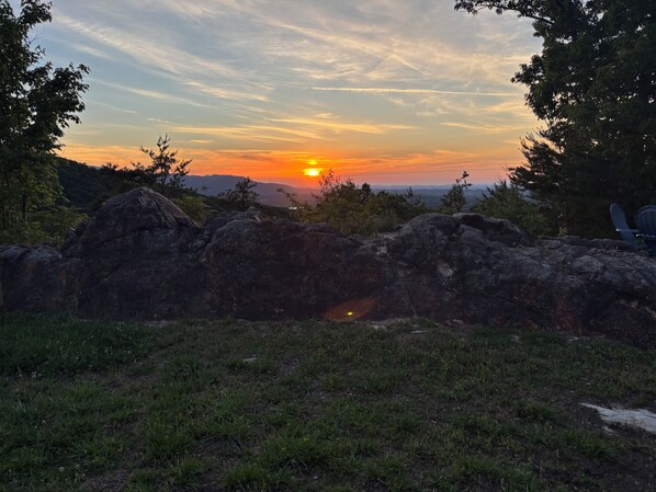 A sunset over a rocky landscape with trees and a chair.