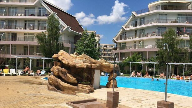 Ein Schwimmbecken mit Felsen, Liegestühlen und einem mehrstöckigen Gebäude im Hintergrund.