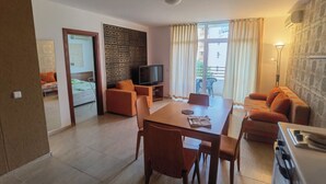 Ein modernes Wohnzimmer mit Essbereich, Fernseher und einem Balkon mit Vorhängen.