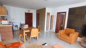 Ein modernes Wohnzimmer mit einer Couch, einem Esstisch mit Stühlen, einer Küchenzeile mit Geräte und einer Wand mit Muster-Tapete.