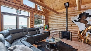 A log cabin interior with a leather sofa, a glass coffee table, a fireplace, and a large window overlooking the sea. - Gorgeous log home in Southern Door- Waterfront retreat (Luxemburg)