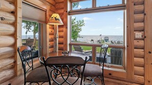 A log cabin interior with a dining table and chairs, a lamp, and a large window offering a view of the sea. - Gorgeous log home in Southern Door- Waterfront retreat (Luxemburg)