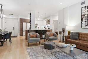 Una sala de estar moderna con un sofá, sillones, una mesa de centro y un comedor con sillas y una mesa.