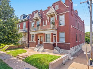A two-story brick building with a front porch, a small balcony, and a fire hydrant in the foreground. - The Urban Botanist-Botanical Garden/ZOO/The Grove/Tower Grove Park (St. Louis)