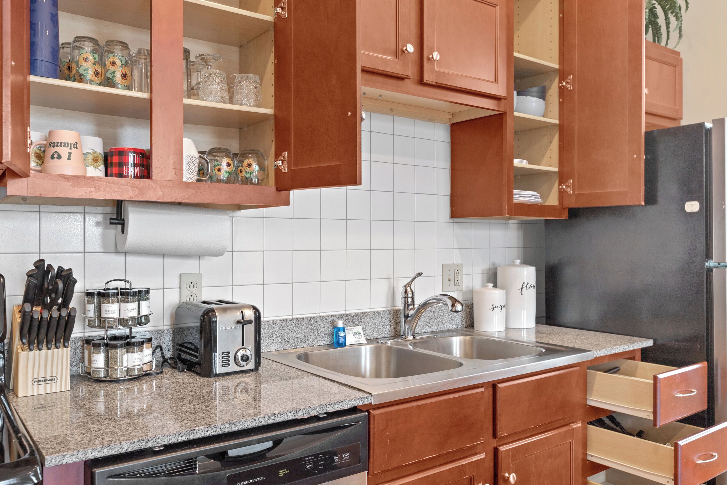 A kitchen with wooden cabinets, a granite countertop, a toaster, a sink, and a dishwasher.