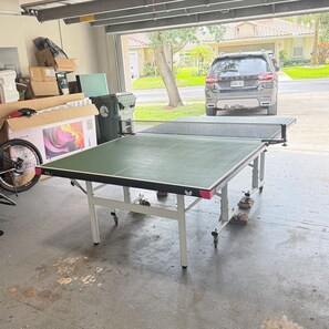 Una mesa de ping pong en un garaje con una bicicleta y cajas.