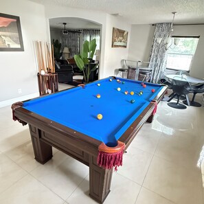A pool table in a room with a dining area, a large plant, and a painting on the wall. - Delightful 2-bedroom house with AC in Coconut Creek (Coconut Creek)