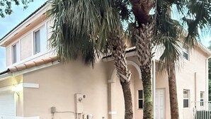 Un edificio residencial con fachada blanca, un garaje y un césped cuidado con dos palmeras.