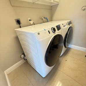 A front-loading washer and dryer in a laundry room with a tiled floor and a white wall. - Delightful 2-bedroom house with AC in Coconut Creek (Coconut Creek)