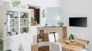 A dining area with a wooden table, white chairs, a white cabinet with glass doors, a brick fireplace, and a flat-screen TV mounted on the wall. - Concettina Apartment sea view for up to 5 people! (Massa Lubrense)