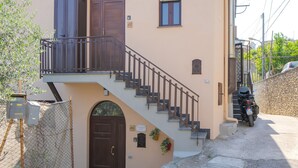 A two-story building with a brown door, a small balcony, and a staircase leading to the upper floor. - Concettina Apartment sea view for up to 5 people! (Massa Lubrense)