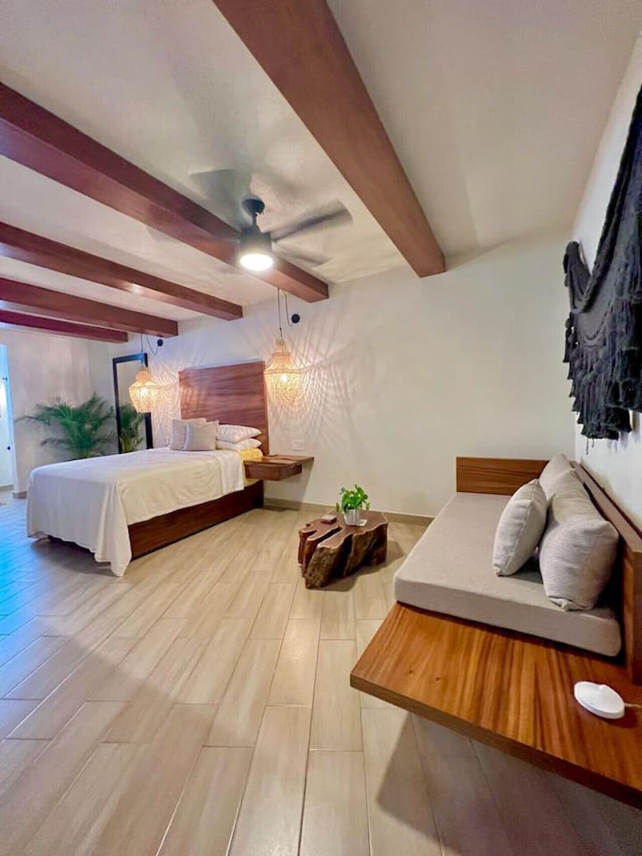A modern bedroom with a bed, a sofa, a wooden coffee table, and a hanging light fixture.