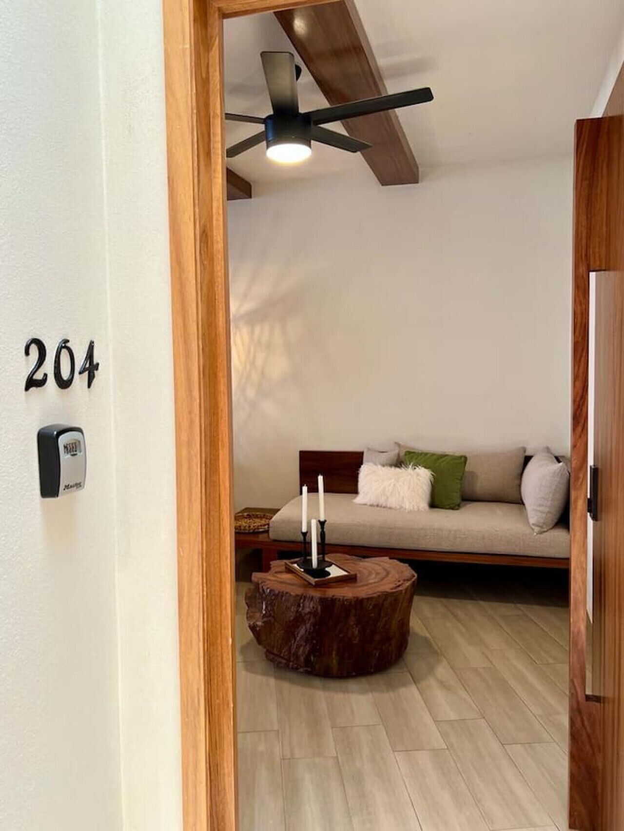 Une pièce avec un ventilateur de plafond, un plancher en bois, un canapé avec des coussins et le numéro « 204 » peint sur le mur.