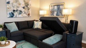 Ein modulares Sofa mit integriertem Stauraumbank, ein kleiner Tisch mit Pflanze und ein Lautsprecher auf einem Schrank.