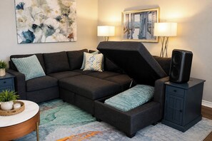 Ein modulares Sofa mit integriertem Stauraumbank, ein kleiner Tisch mit Pflanze und ein Lautsprecher auf einem Schrank.