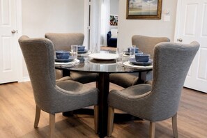 Un coin repas avec une table ronde, quatre chaises grises à revêtement rembourré et une porte blanche en arrière-plan.