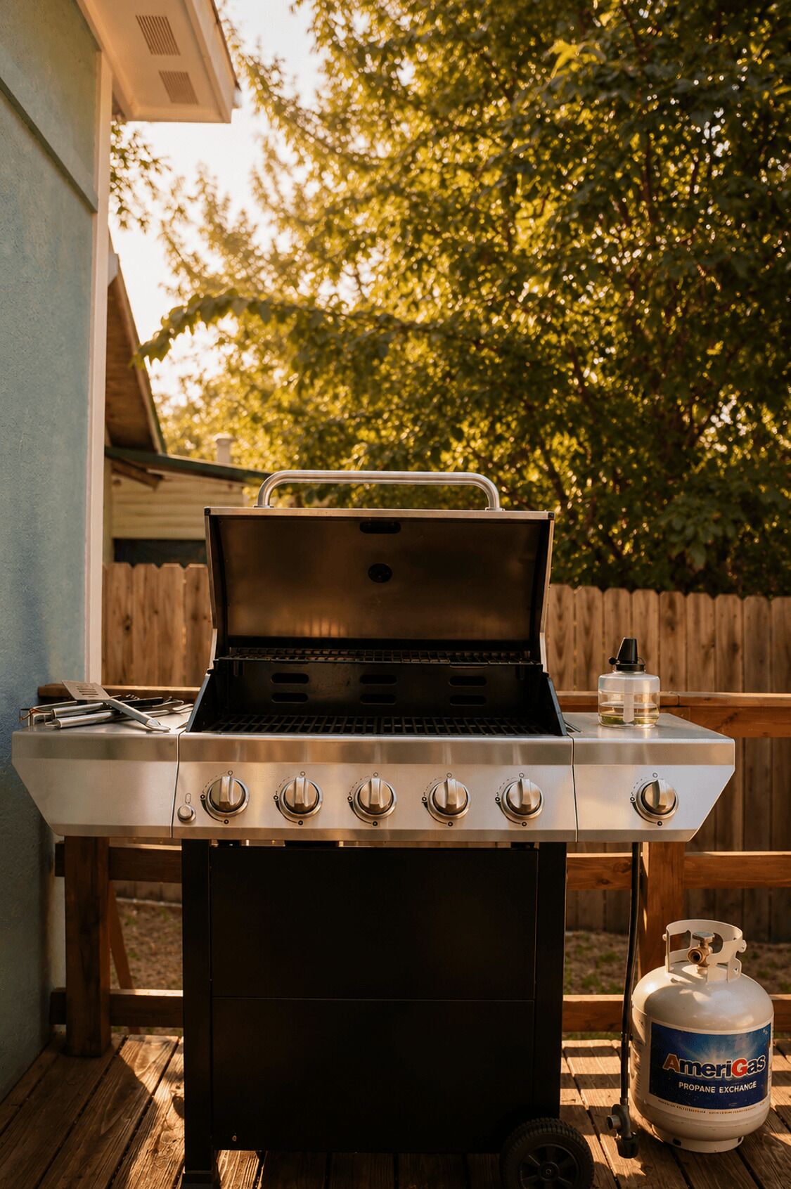 A portable gas grill with five burners and a propane tank on a wooden deck.